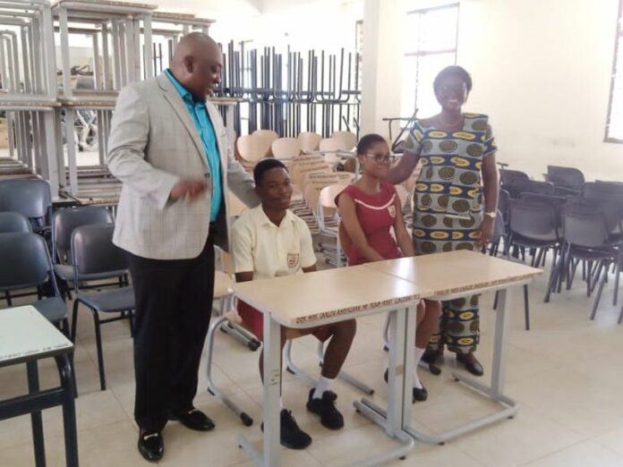 Carlos Ahenkorah and Mrs Vida Antwi in a group picture with two students seated on the new furniture at the Lashibi Community SHS