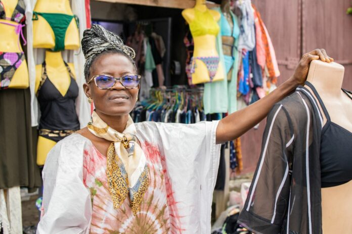 Bernadette stands in front of her business in Cameroon established with support from IOM after returning from Libya.