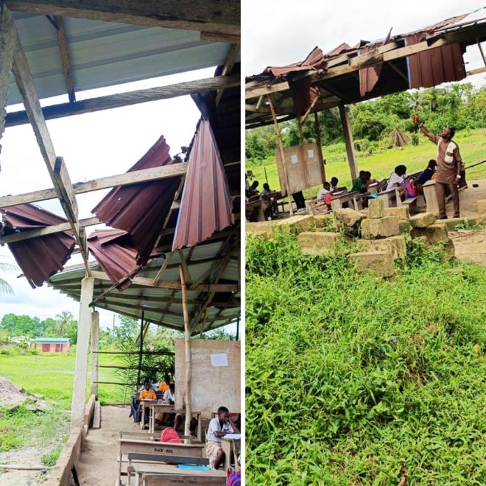 A concern parent pointing to the dilapidated structure of the school; Roofing sheets hanging loosely