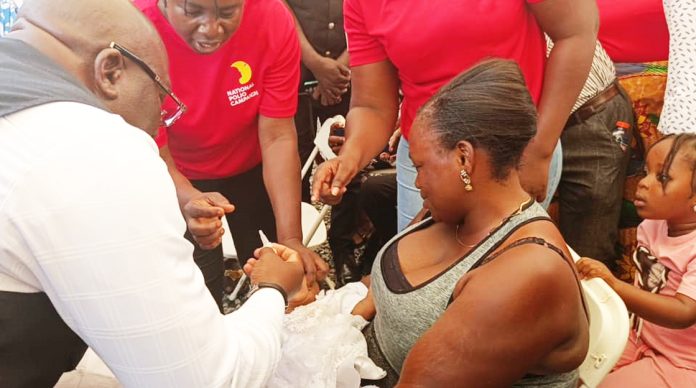 The Eastern Regional Minister Hon. Seth Kwame Acheampong (with his back to the camera) in a ceremonial immunizilization of a child at the programme.