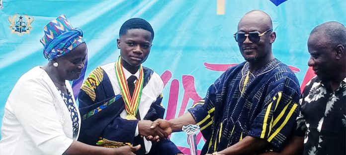 Overall Best Student Lord Kumi (middle) receiving his Prize from the Municipal Education Director Mr. Koomson (right)