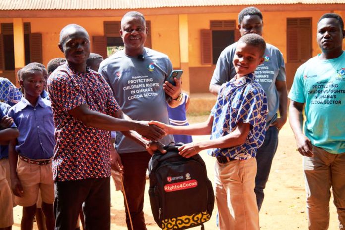 A beneficiary pupil receiving his pack the school head. In the middle is the CEO of GLOMEF Ghana