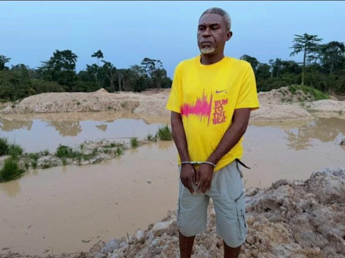 Elder David Bobie Peter in handcuffs after his arrest by NAIMOS over his alleged involvement in illegal mining (galamsey).